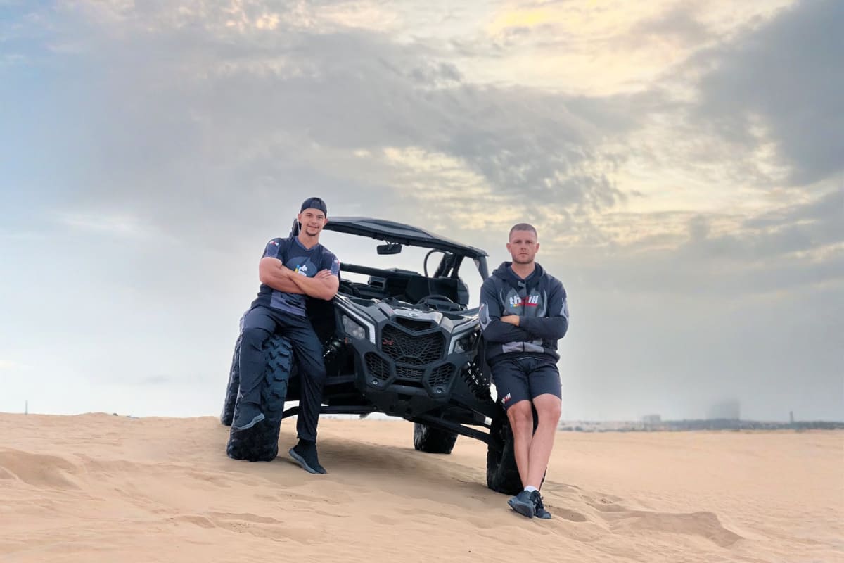 Two riders in a Can-Am Maverick buggy kicking up dust while driving across golden sand dunes in the desert (2)