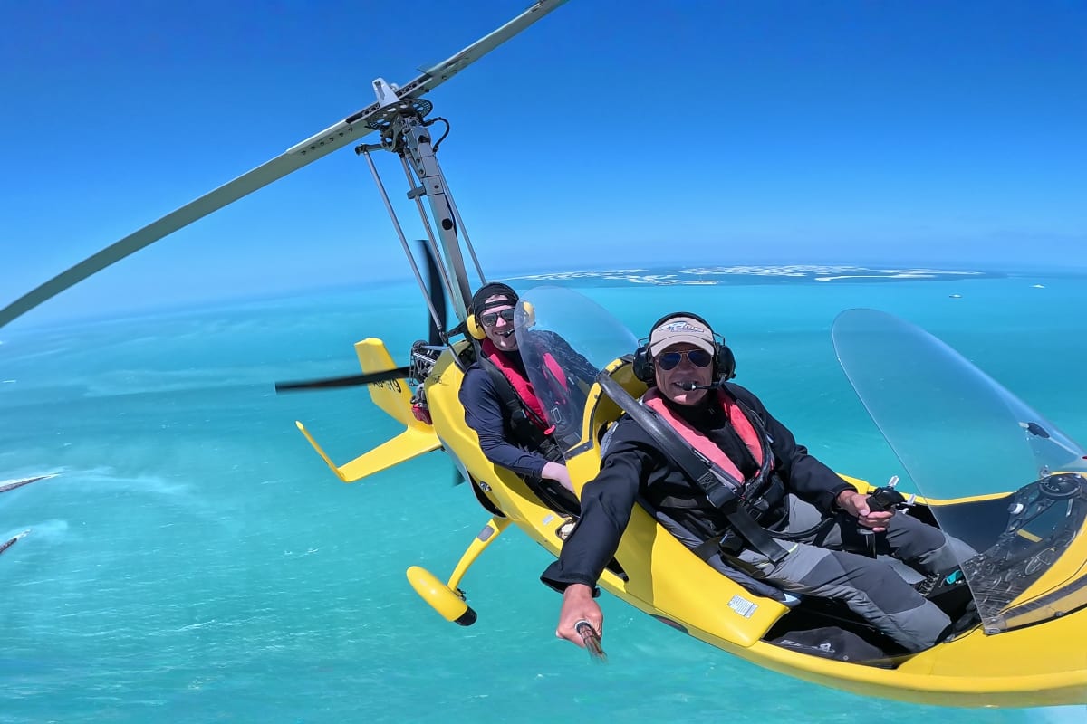 Yellow gyrocopter flying over Dubai cityscape with Burj Khalifa and modern skyscrapers visible below against blue sky (2)