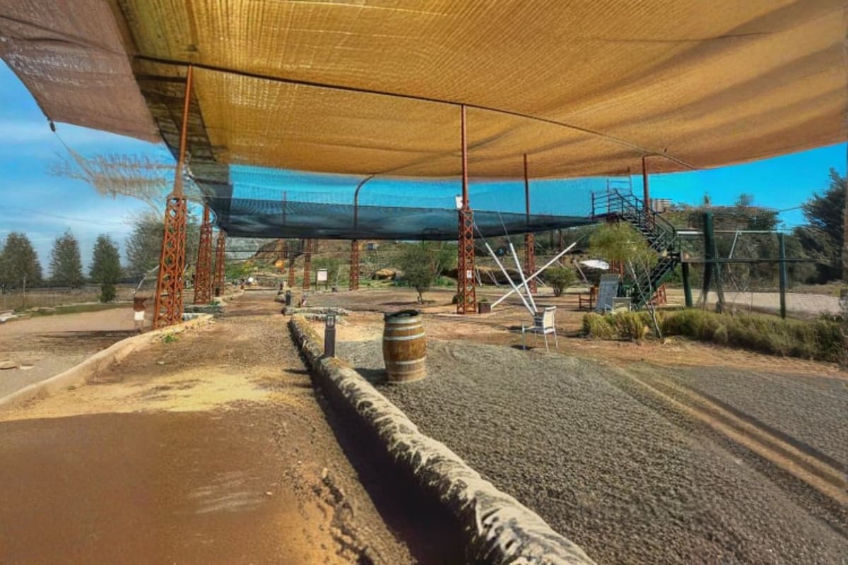 Person zip-lining across obstacle course with metal beams and stone towers at adventure park in mountainous landscape (4)