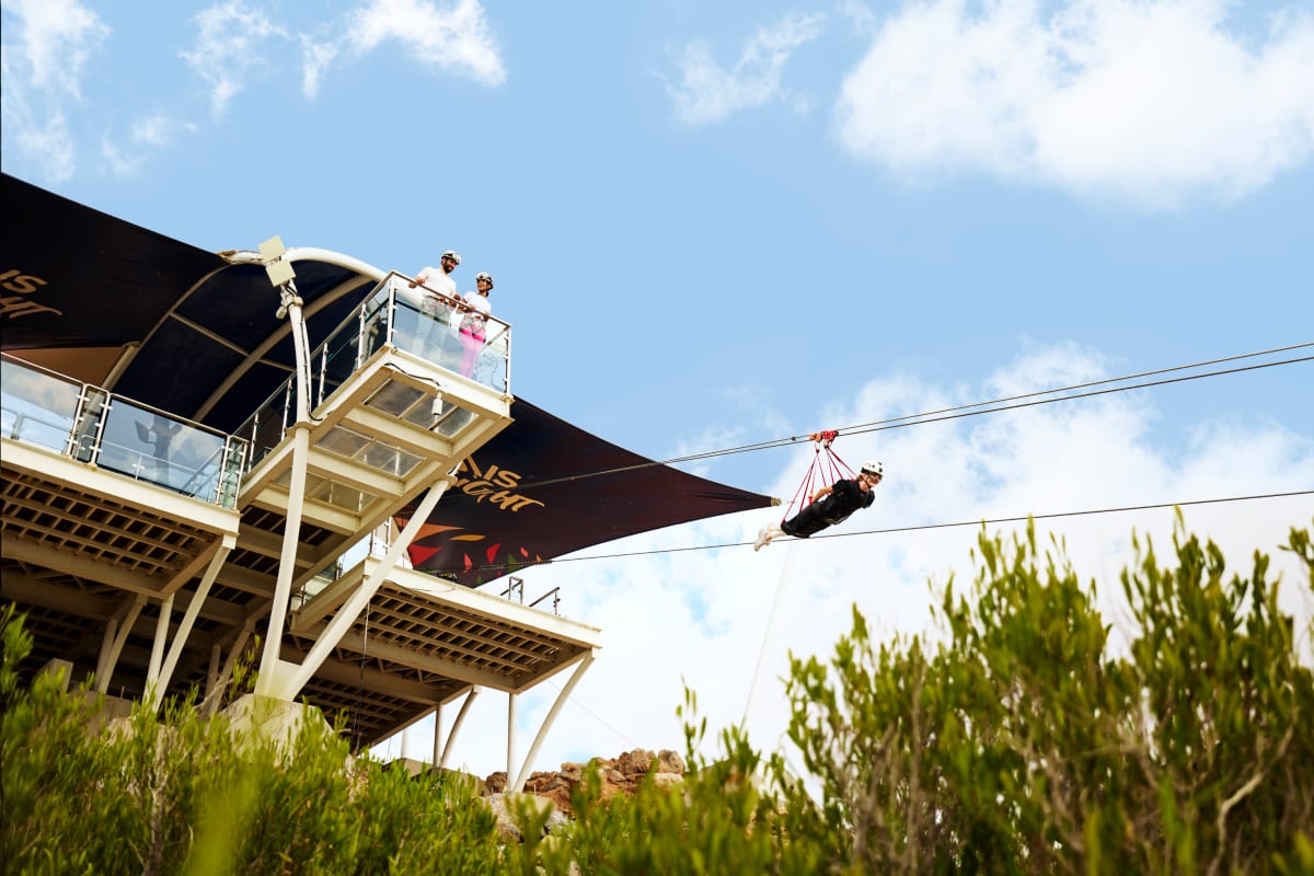 Person zip-lining across cables from elevated platform at Jebel Jais with desert landscape and blue sky below