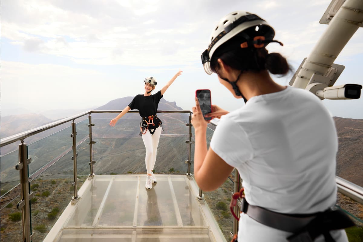 Person zip-lining across cables from elevated platform at Jebel Jais with desert landscape and blue sky below (2)