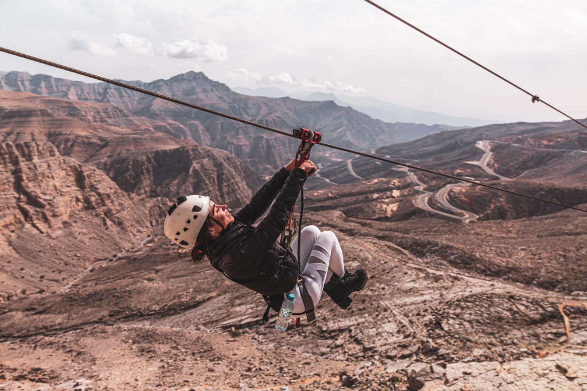 Person zip-lining across cables from elevated platform at Jebel Jais with desert landscape and blue sky below (5)