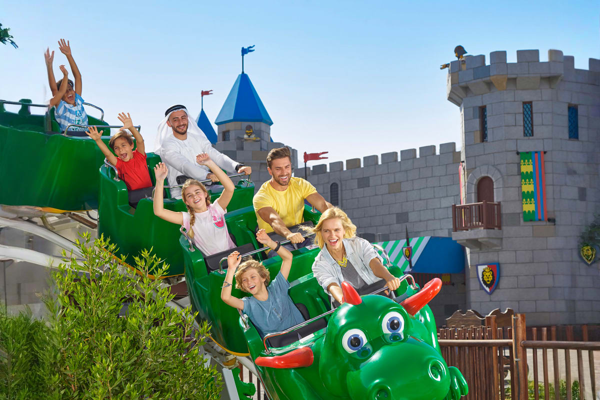 Family running outside LEGO Factory building at Legoland Dubai with colorful brick facade and large gear sign (2)