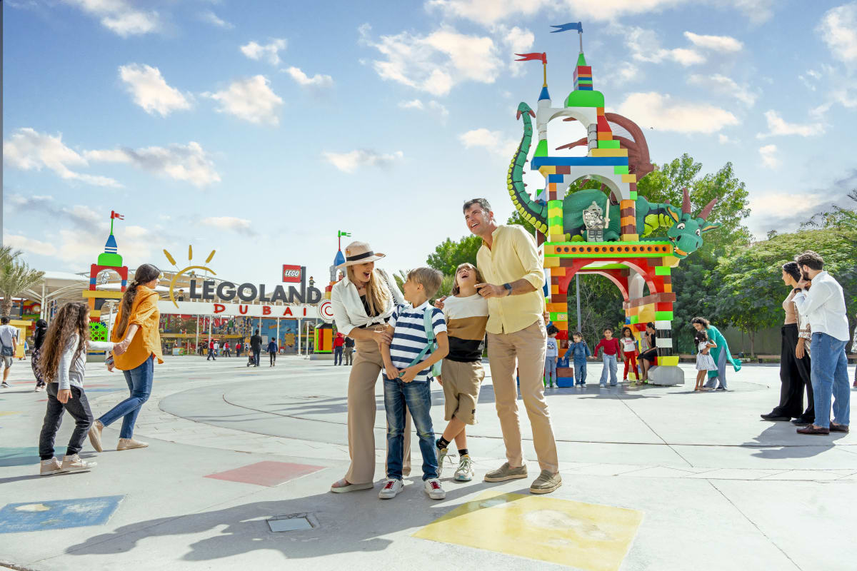 Family running outside LEGO Factory building at Legoland Dubai with colorful brick facade and large gear sign (4)