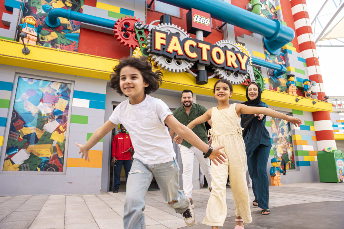 Family running outside LEGO Factory building at Legoland Dubai with colorful brick facade and large gear sign