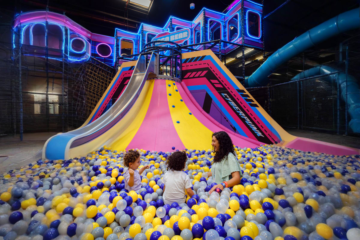 Group of eight people posing at a bowling alley with a blue bowling ball on the lane, purple and pink neon lighting (5)