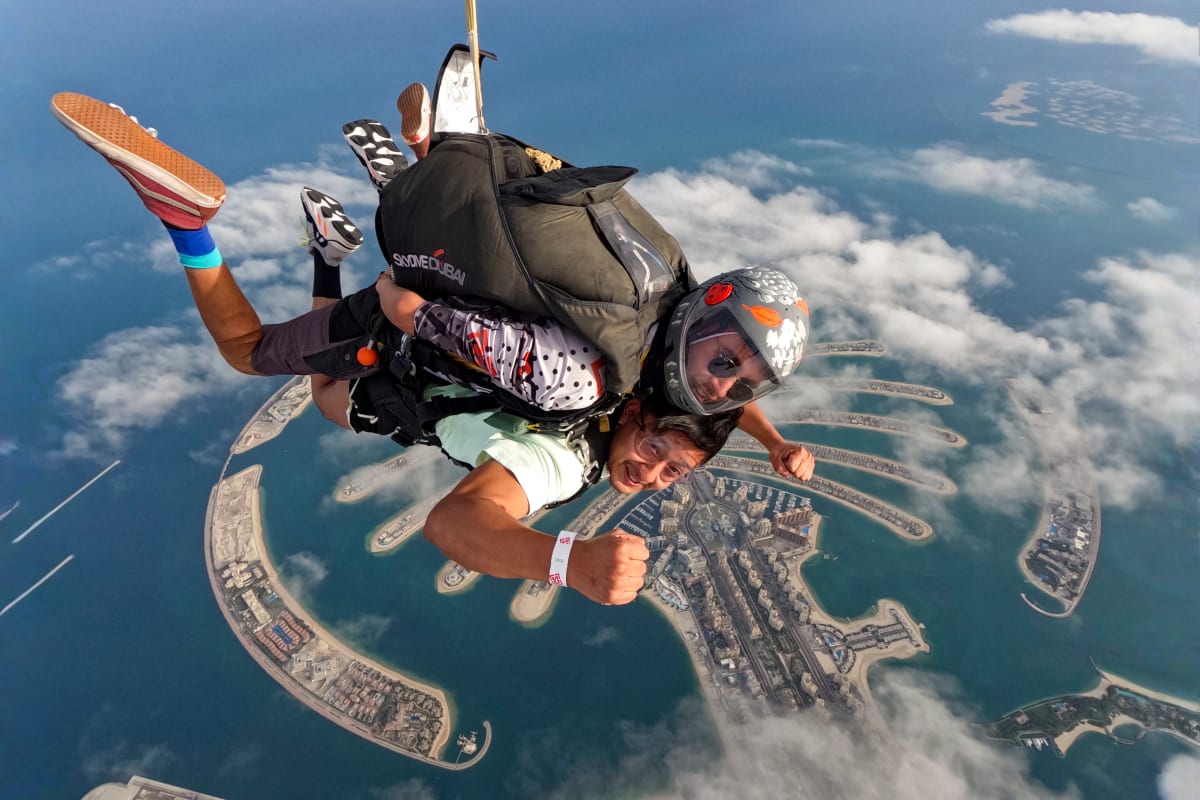 Skydiver in freefall above Palm Jumeirah with tandem instructor, showing Dubai's iconic palm-shaped islands and turquoise water